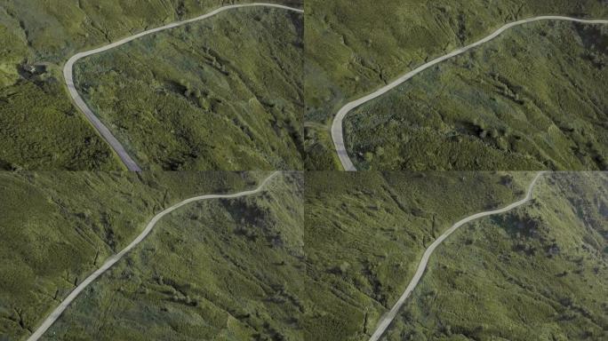 Pan拍摄了一条弯曲的道路，该道路建在被岩石和绿色植物包围的山上