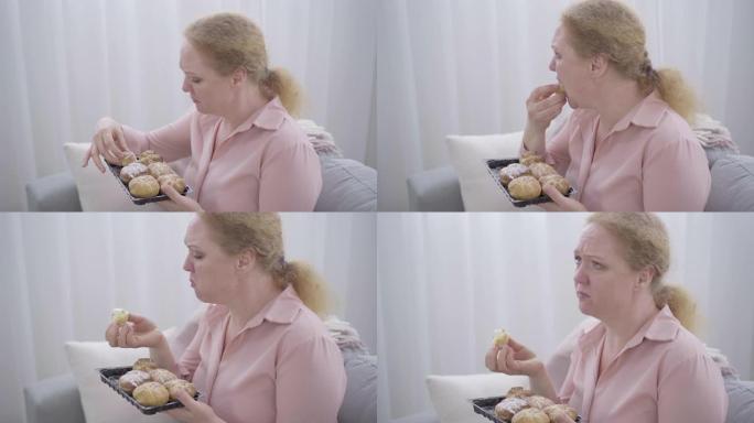 沮丧的胖乎乎的女人嚼着甜面包，哭了起来。紧张的高加索高级女士抑郁症的侧视图。悲伤，垃圾食品，压力饮食