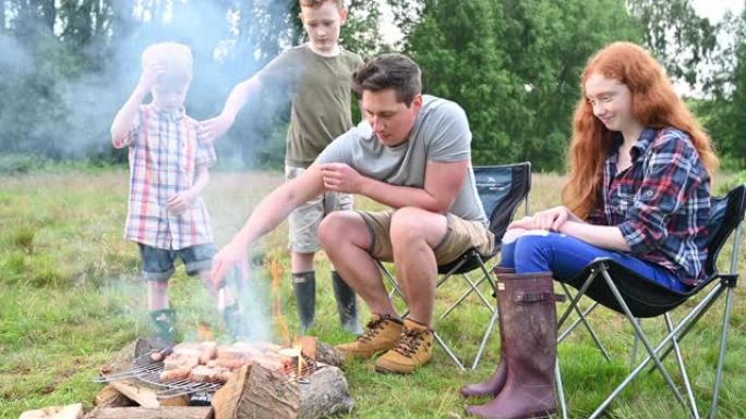 孩子们看着单身父亲在热篝火上烧烤食物