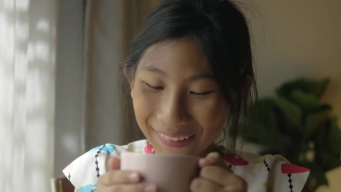 昏昏欲睡的亚洲女孩在清晨在家窗户附近喝一杯热巧克力，生活方式概念。
