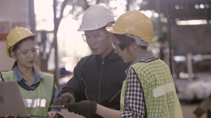 团队工程和工人使用笔记本电脑在重工业制造工厂工作时佩戴个人防护设备。在装配和生产线上一起谈论计划项目