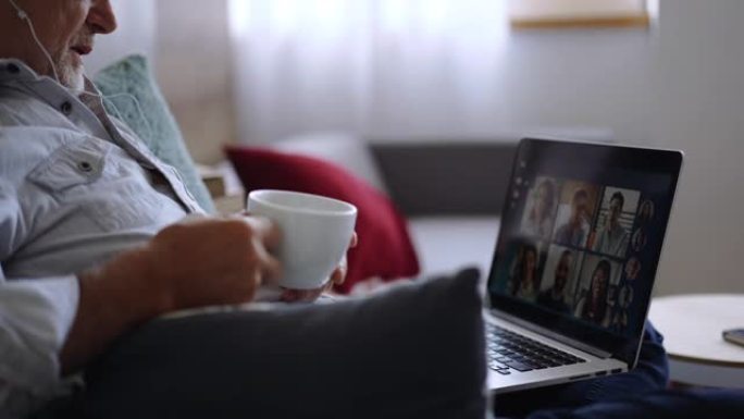 老年男子在沙发上视频聊天时喝咖啡