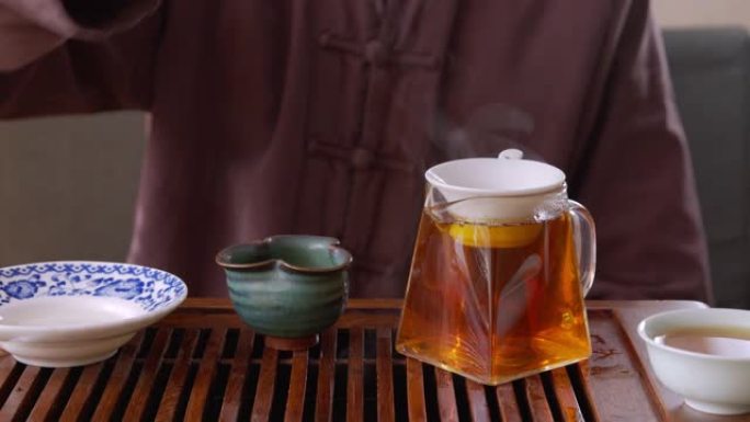 茶师傅将新鲜的泡茶从盖湾倒入筛子到玻璃杯壶中。男子在传统仪式上将热茶饮料倒入托盘上的茶壶中。