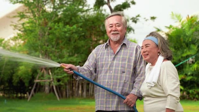 亚洲老年夫妇正在用橡胶管给后院的植物浇水。老年人的爱好