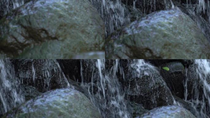 封闭垂直的白水在人造瀑布级联的岩石表面上流动，前景中覆盖着深绿色藻类的湿滑巨石。