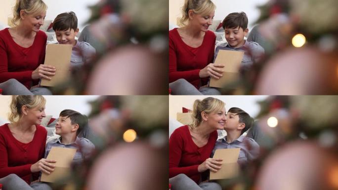 圣诞快乐，家庭幸福，儿子感谢圣诞节礼物，在客厅的照亮和装饰的树附近给妈妈一个吻