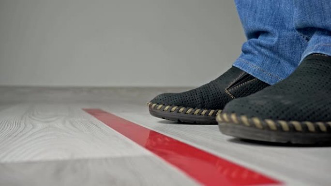 靠近地板上的红色条，一个人的孤立的鞋子和腿的特写，排队等候并保持距离。在新型冠状病毒肺炎期间