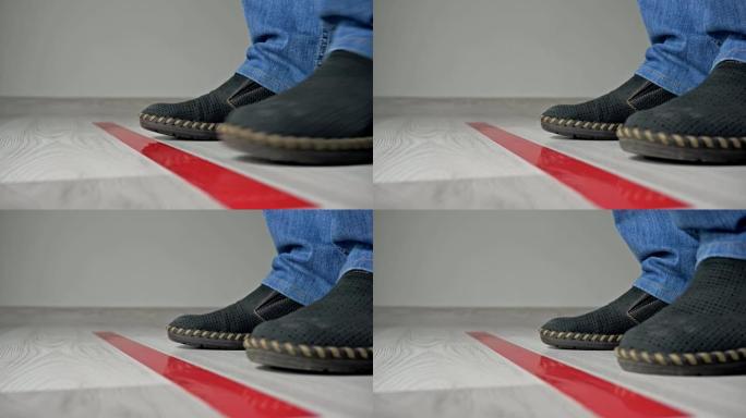 靠近地板上的红色条，一个人的孤立的鞋子和腿的特写，排队等候并保持距离。在新型冠状病毒肺炎期间