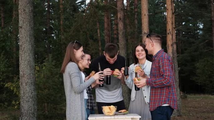 一群朋友在大自然中休息和放松。人们吃汉堡，喝啤酒，交流和欢笑。