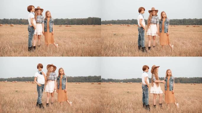 十几岁的朋友站在草堆背景下的乡下田野上。男孩和两个女孩在秋村的收割场上摆姿势。