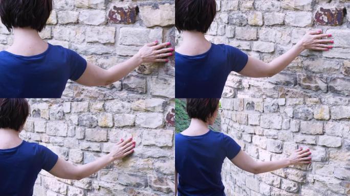 女人用手滑向古老的石墙。在古老美丽的欧洲城市中，女性的手触摸坚硬的岩石表面。感性的触摸。坚硬的石头表