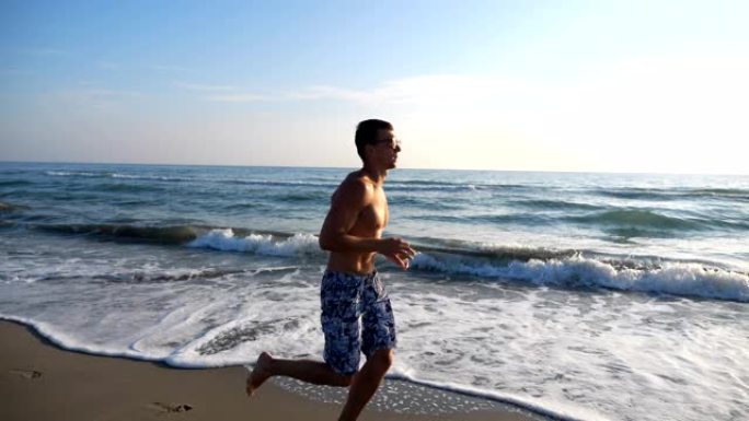 运动帅哥在海岸慢跑，背景是美丽的海景。年轻的运动型男子在晚上沿着海洋海滩奔跑。在海边做运动的男运动员