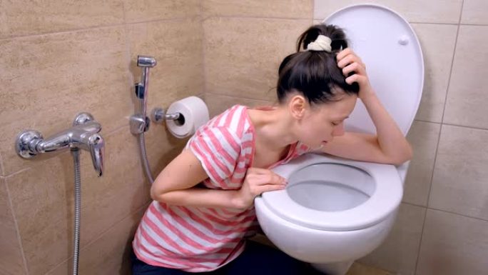 喝醉的女人在厕所里呕吐，坐在家里的地板上，宿醉，侧视图。