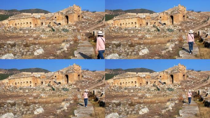 年轻女子单人旅行者在土耳其棉花堡的希拉波利斯古城为圆形剧场拍照