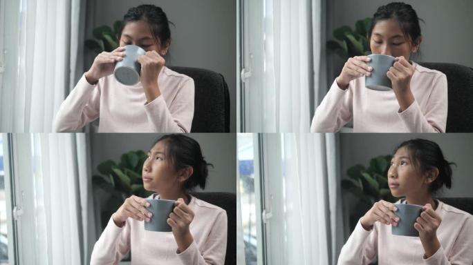 亚洲女孩在灰色马克杯里喝热巧克力，在雨天在家看着窗外，生活方式理念。