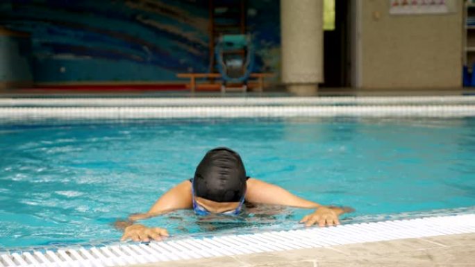 年轻女子游出水面，在室内游泳池摘下安全眼镜