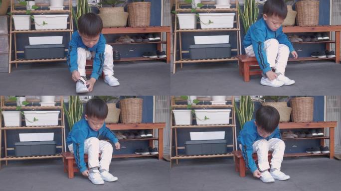 亚洲3岁幼稚园孩子坐在靠近他家前门的鞋架，集中精力穿上他的白色鞋子/运动鞋