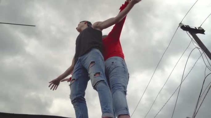 一个年轻人和一个女孩在摩天大楼的屋顶上对着天空跳舞。