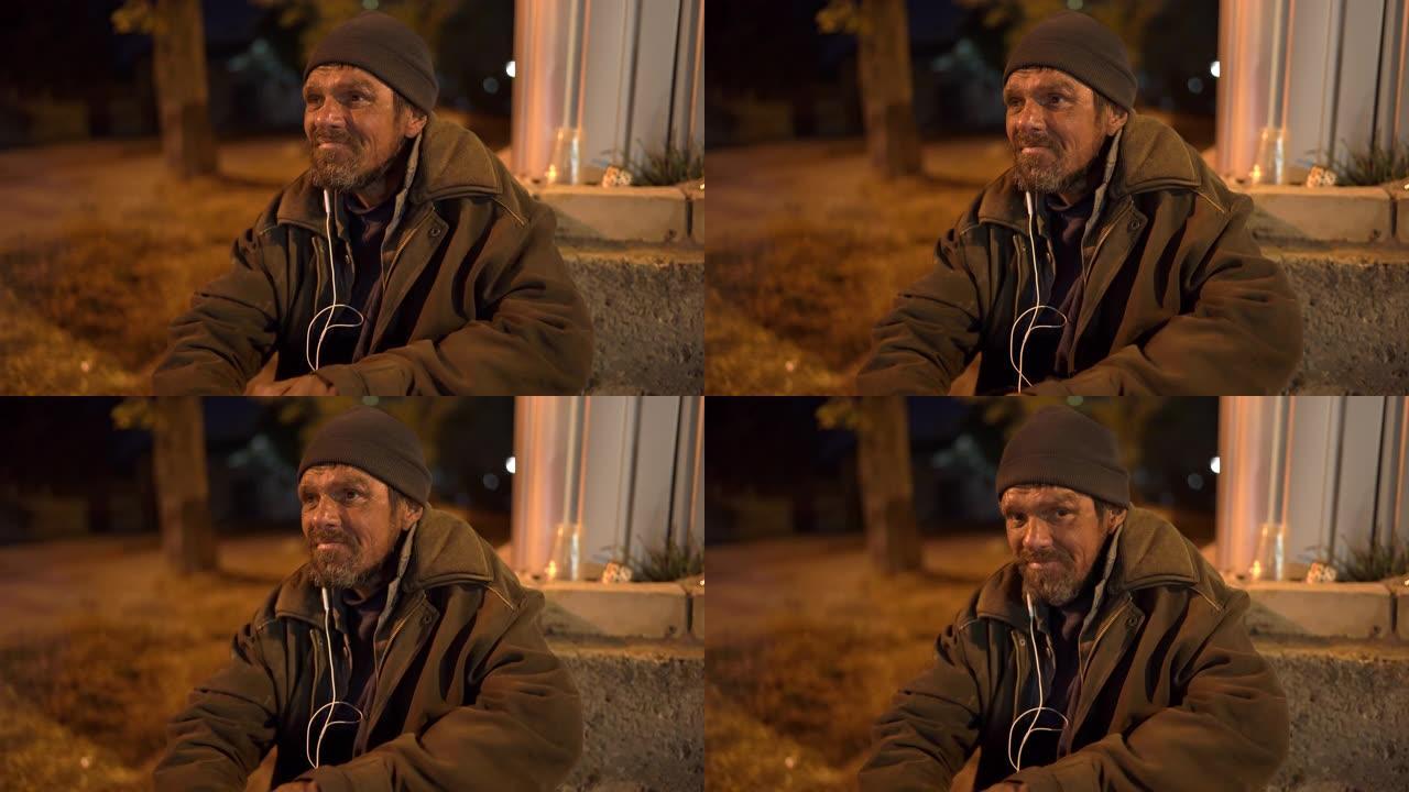 无家可归的人晚上坐在街上使用耳机。