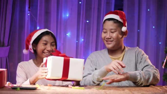 戴着圣诞老人帽子的亚洲男孩和女孩在家里互相交换礼品盒，圣诞灯背景。