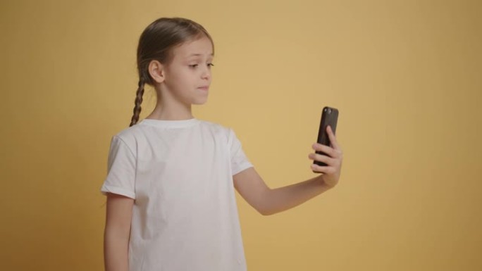 女孩在黄色背景下使用智能手机在视频聊天中聊天慢动作