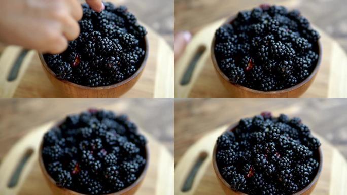 女人的手将黑莓放在木桌上的碗中