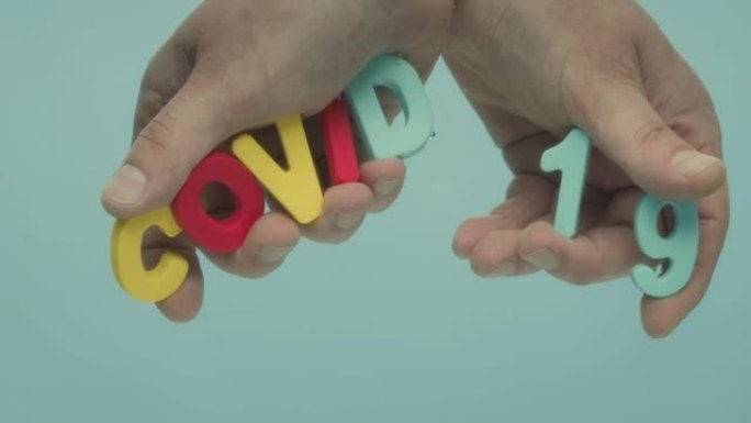 两只手握着用塑料字母制成的单词 “COVID 19”。