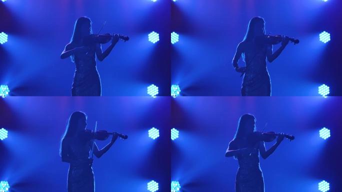 小提琴上古典旋律的现场演奏。聚光灯下蓝色背景下烟雾中的女人的剪影。慢动作。特写