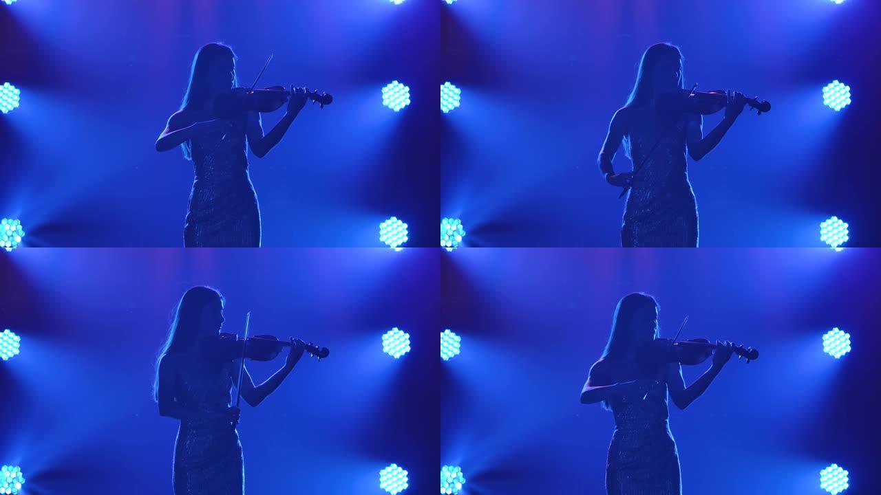 小提琴上古典旋律的现场演奏。聚光灯下蓝色背景下烟雾中的女人的剪影。慢动作。特写