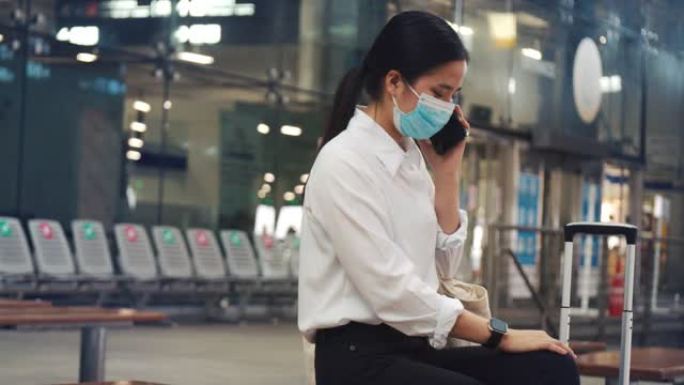 女商人戴着外科口罩保护，在机场候机楼与朋友通电话，并在新型冠状病毒肺炎大流行期间保持社交距离。