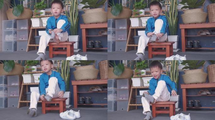 亚洲3岁幼稚园的孩子坐在靠近他家前门的鞋架，集中精力穿上自己的袜子