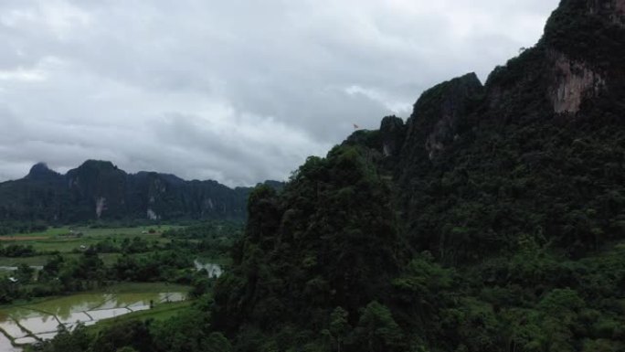 在雨中季风期间，自然界的风景在老挝万英的稻田和树木繁茂的山脉中，喀斯特峰上有一面老挝国旗。