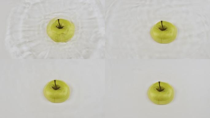 绿色的苹果片落在白色的水中。慢动作。