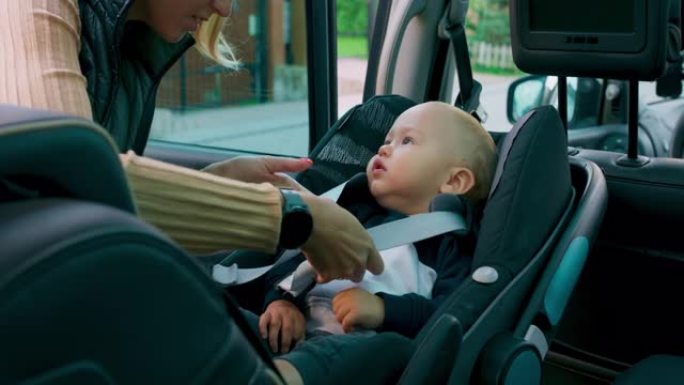 车内摄像头。特写婴儿汽车座椅。男婴出现在他母亲的手上，母亲将婴儿放在婴儿汽车座椅内。母亲对他微笑，系