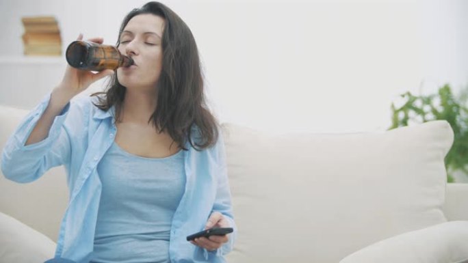 Slowmo. Tipsy的黑发女人正在通过智能手机聊天，拿着一瓶啤酒并喝着它。