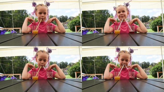 一个有着不同寻常美丽发型的女孩正坐在夏季咖啡馆的一张桌子旁。孩子通过管子喝果汁。女孩一次喝了三杯五颜