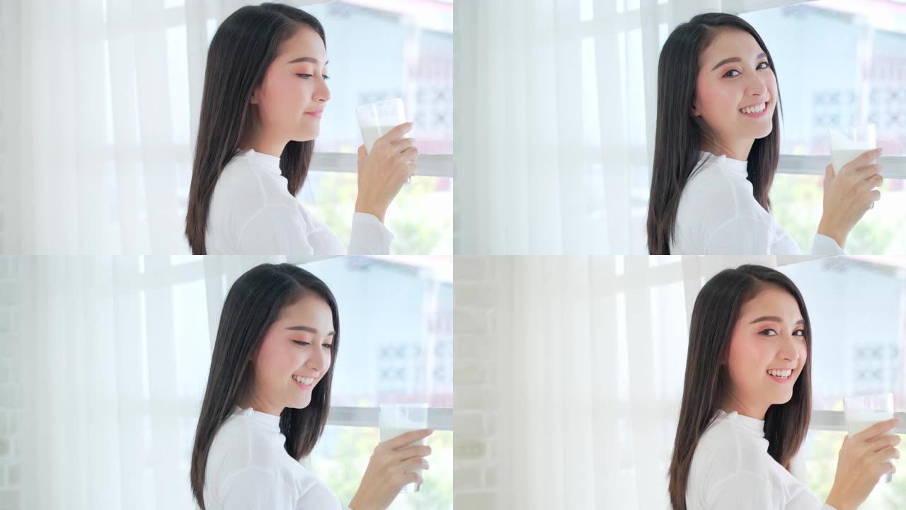 迷人的亚洲女性喝牛奶，在家微笑。健康的生活方式。