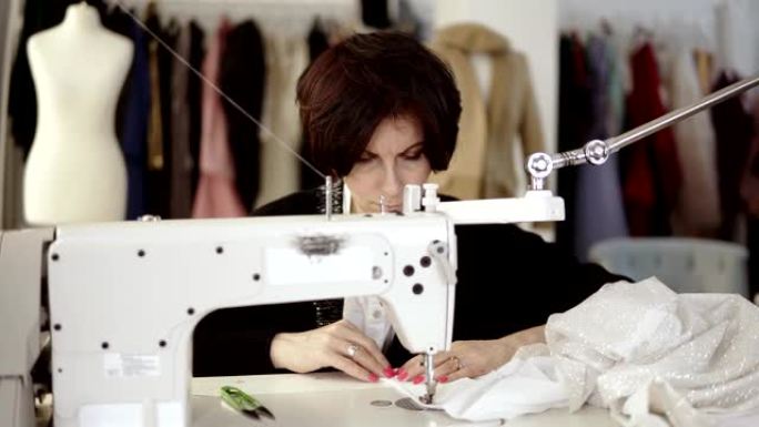 成年女性的肖像女裁缝在缝纫机上工作，穿着白色手工制作的衣服。时尚服装和背景上的白色人体模型