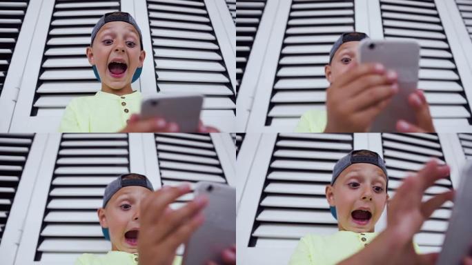 有趣可爱的小男孩在智能手机上玩游戏。5-6岁的小男孩拿着手机离他的脸太近了。电话在线游戏中男孩的情绪