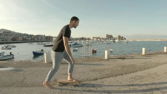 穿着牛仔裤和黑色短袖t恤的年轻人在大海为背景的码头上赤脚滑冰