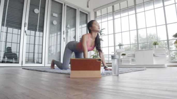 穿着运动服的美丽亚洲女性在家客厅的垫子上做伸展瑜伽锻炼。