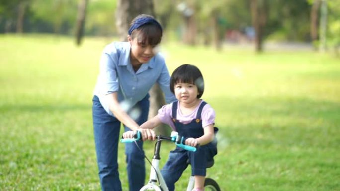 亚洲小女孩勒宁和年轻的母亲在花园里骑自行车