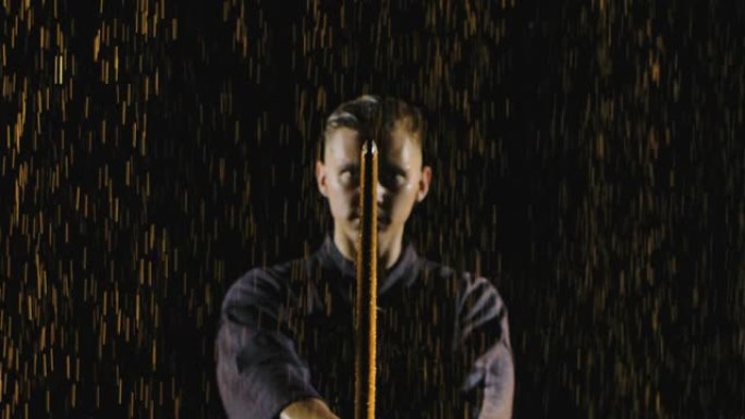 一名日本剑道战士将他的神井降向相机的肖像。在雨中拍摄在黑色背景上。特写。慢动作