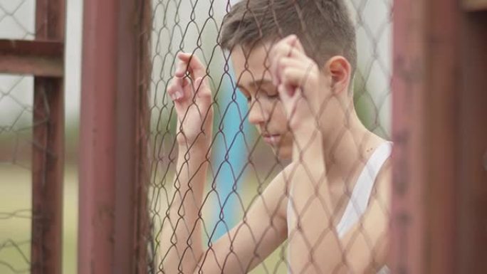 孤儿难民男孩独自一人低头在篱笆附近