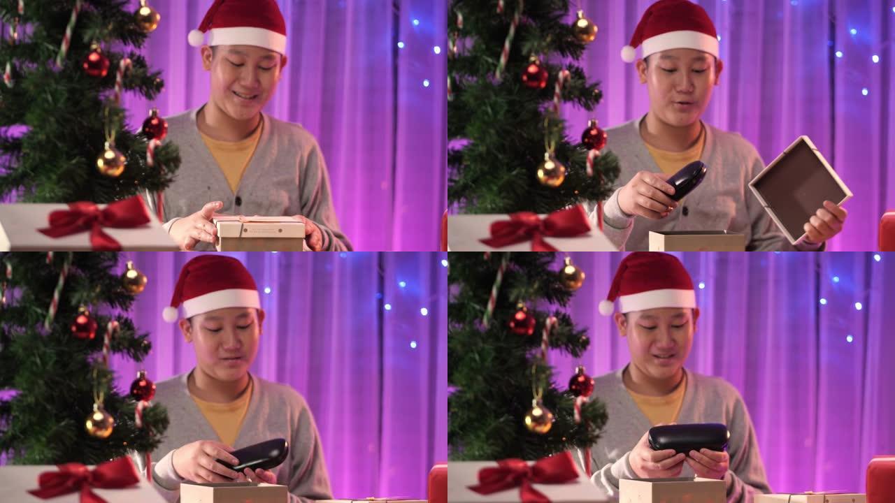 快乐的亚洲男孩戴着圣诞老人帽子打开礼品盒与圣诞灯背景。