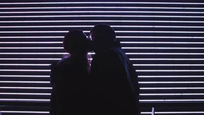 年轻的男人和女人在夜街热情地亲吻，大都市的灯光