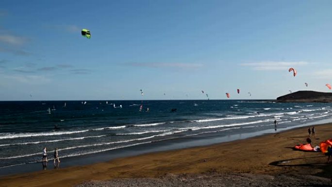 在大风天，海滩上有许多五颜六色的风筝和风筝冲浪者乘风破浪