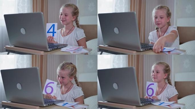 在家中的在线教育，女孩在用笔记本电脑从家里学习学校课程数学给女老师看带有数字的卡片
