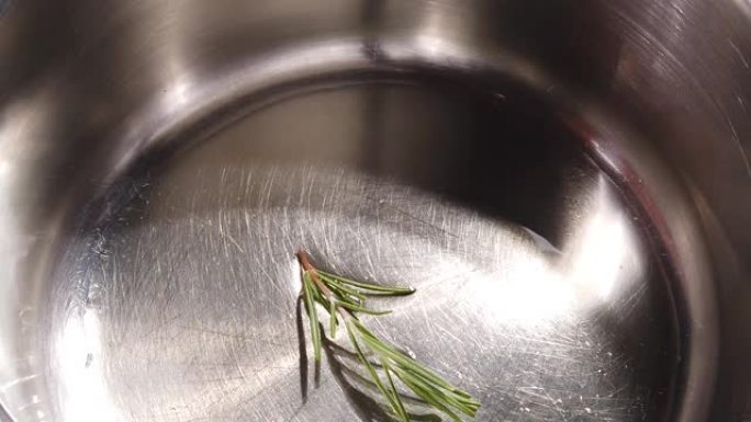 将新鲜迷迭香树枝倒入不锈钢锅中的热油中的慢动作高角度