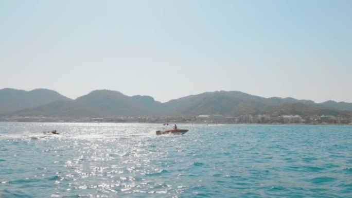 摩托艇在山上和城市背景下的海上乘坐旅游充气管。乘坐黄色充气香蕉的海船。暑假的水上运动活动。